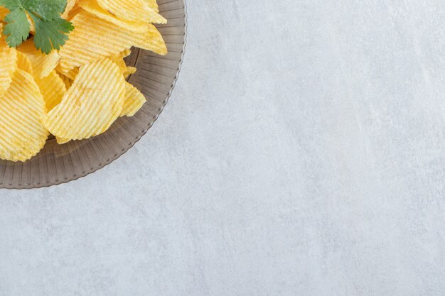 Assiette en verre de savoureux chips d'ondulation sur pierre.