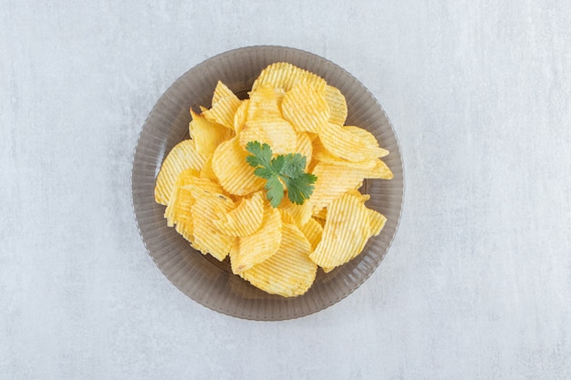 Assiette en verre de savoureux chips d'ondulation sur pierre.