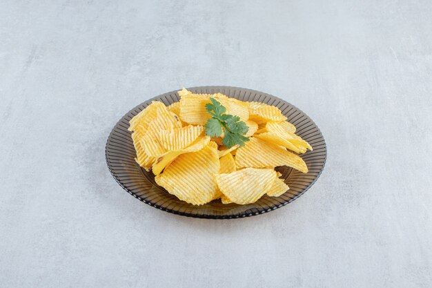 Assiette en verre de savoureux chips d'ondulation sur pierre.