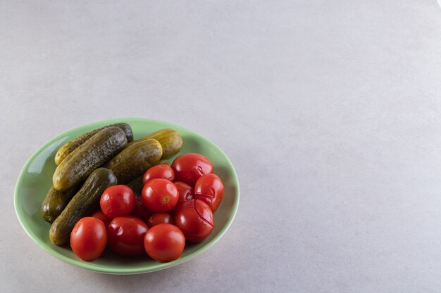 Assiette verte de concombres et tomates marinés sur table en pierre.