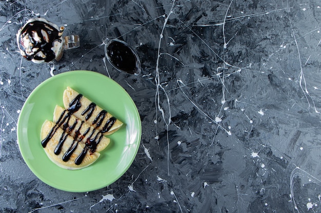 Assiette verte de crêpes maison avec garniture au chocolat et verre de café glacé.