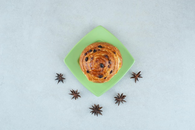 Une assiette verte de pâtisserie et d'anis étoilé sur table blanche.