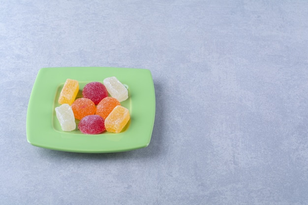 Une assiette verte pleine de bonbons à la gelée sucrée sur une surface grise