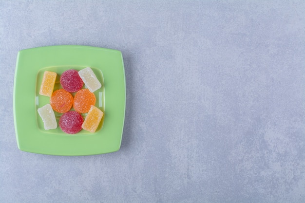 Une assiette verte pleine de bonbons à la gelée sucrée sur une surface grise