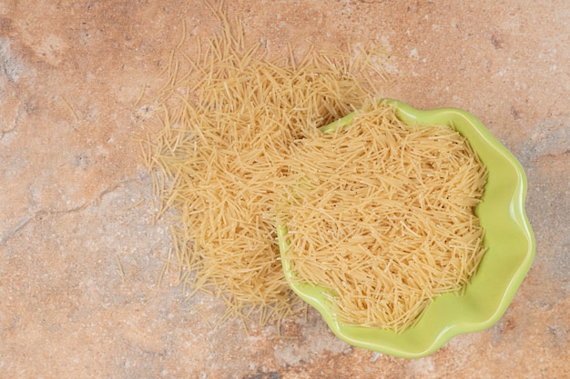 Photo gratuite une assiette verte pleine de petits vermicelles sur fond de marbre. photo de haute qualité