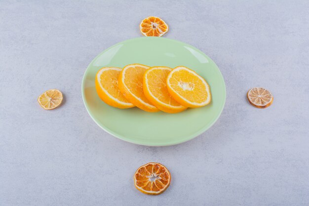Assiette verte de tranches d'orange fraîche sur table en pierre.