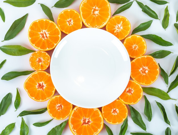 Photo gratuite assiette vide entourée de fruits et de feuilles d'orange vue de dessus