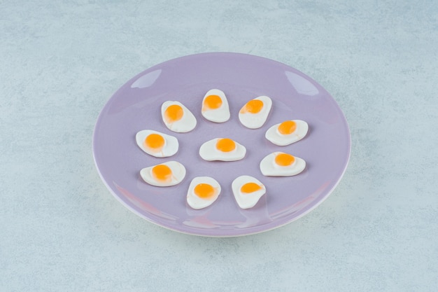 Photo gratuite une assiette violette de bonbons sucrés à la gelée d'œufs brouillés sur une surface blanche