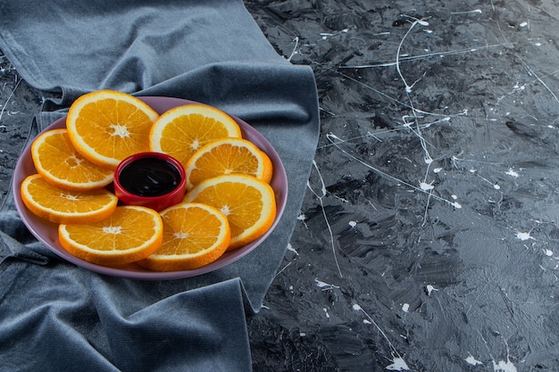 Photo gratuite assiette violette d'oranges juteuses tranchées sur une surface en marbre.