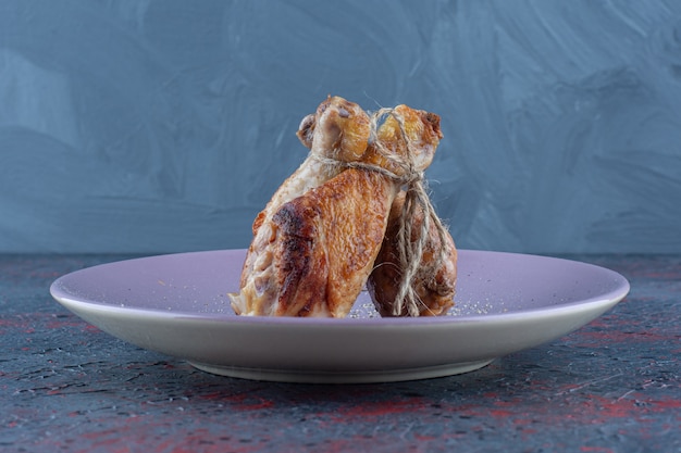 Une assiette violette avec de la viande de cuisses de poulet en corde.