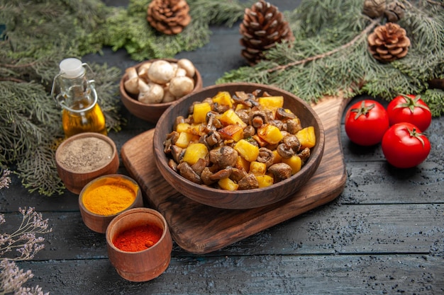 Photo gratuite assiette de vue de dessus et assiette de légumes de pommes de terre et de champignons sur une planche à découper en bois à côté de trois tomates et différentes épices sous l'huile dans des branches d'arbres en bouteille et un bol de champignons