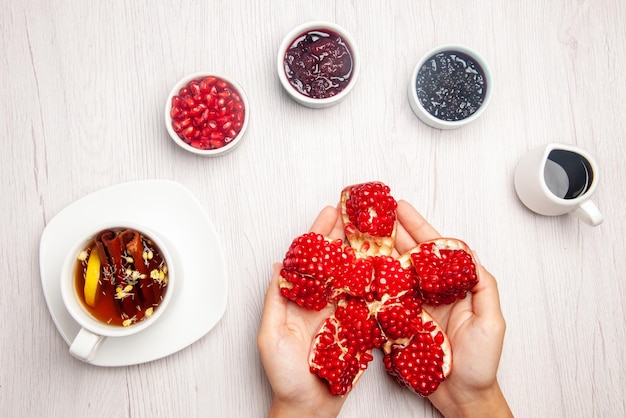 Assiette vue de dessus sur la table blanche grenade pelée dans les mains des bols de confiture et de sauce et une tasse de tisane au citron sur la table