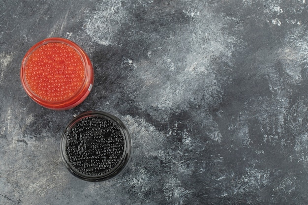 Assiettes en verre pleines de caviar rouge et noir sur une table en marbre.