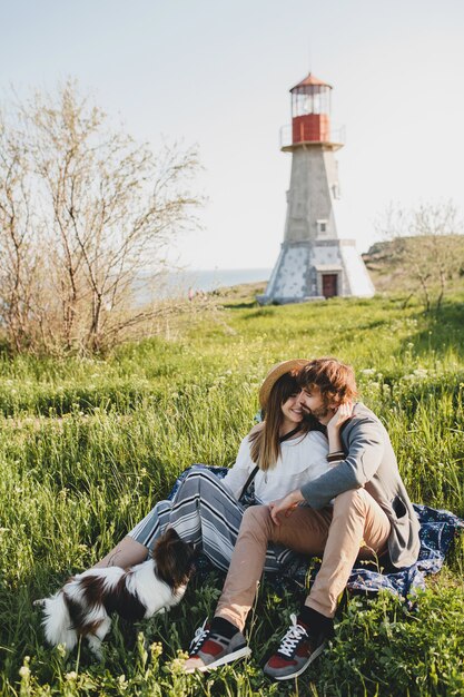 Assis dans l'herbe jeune couple hipster élégant amoureux marchant avec un chien dans la campagne