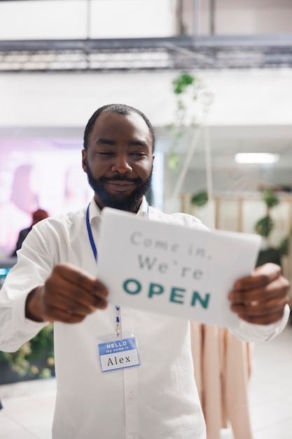 Photo gratuite assistant de magasin de mode accroché à un panneau d'ouverture sur la fenêtre de la boutique