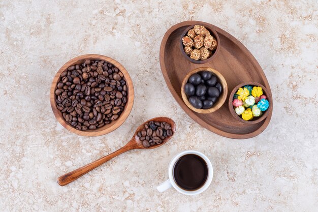 Assortiment de collations dans un plateau en bois à côté de grains de café et une tasse de café infusé