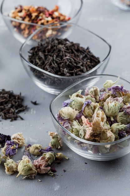 Assortiment d'herbes séchées dans des bols en verre gros plan sur une surface en plâtre