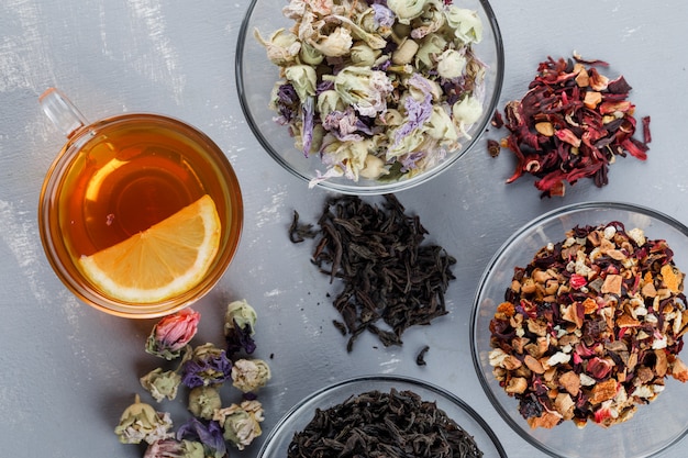 Assortiment D'herbes Séchées Dans Des Bols En Verre Avec Une Tasse De Thé à Plat Sur Une Surface En Plâtre