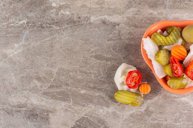 Assortiment de légumes cornichons dans un bol placé sur une table en pierre.