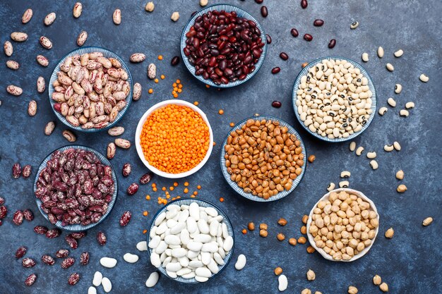 Assortiment de légumineuses et de haricots dans différents bols sur une surface en pierre claire. Vue de dessus. Nourriture protéinée végétalienne saine.