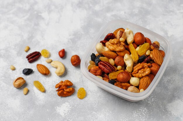 Assortiment de noix dans un récipient en plastique. Noix de cajou, noisettes, noix, pistache, pacanes, pignons de pin, cacahuètes, raisins secs.