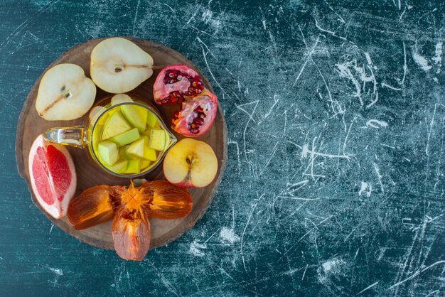 Un assortiment de tranches de fruits sur une planche avec du jus naturel dans une carafe de jus et de pomme sur le fond bleu. Photo de haute qualité