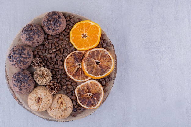 Assortiment de tranches d'orange sèches et juteuses, grains de café, pommes de pin et biscuits sur une planche sur fond blanc.