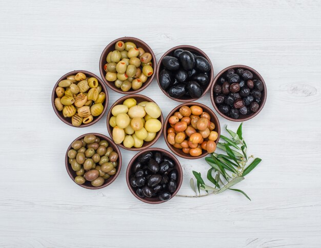 Assortiment de variétés d'olives dans des bols en argile avec des feuilles d'olivier vue de dessus sur bois blanc
