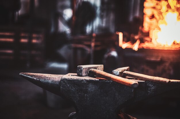 Atelier de stithy sombre avec marteau sur enclume au premier plan et feu dans le poêle à l'arrière-plan.