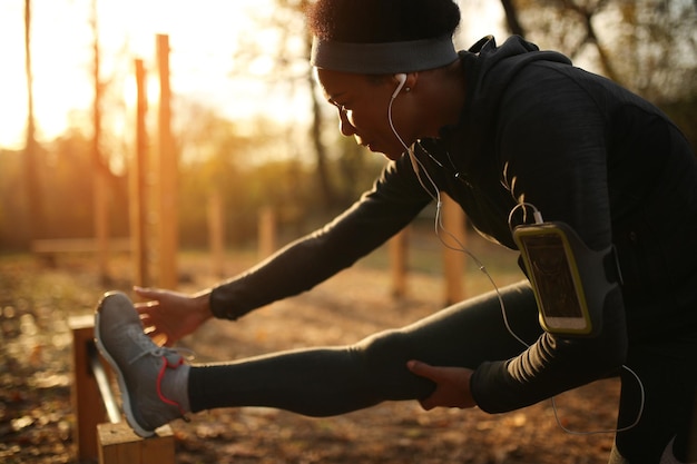 Athlète féminine afro-américaine faisant des exercices d'étirement dans la nature au coucher du soleil