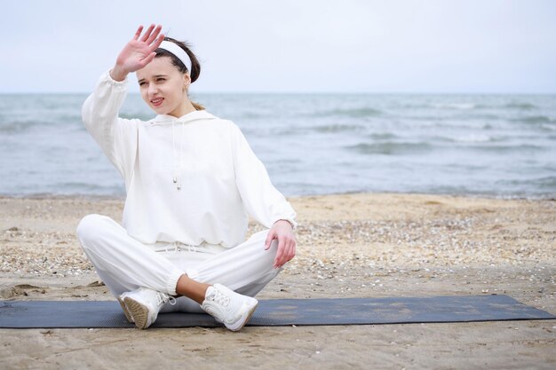 Athlète féminine assise à la plage sur le tapis et leva la main Photo de haute qualité