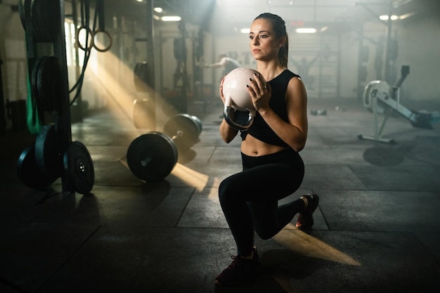 Athlète féminine avec kettle bell pratiquant la fente sur l'entraînement croisé dans un club de santé