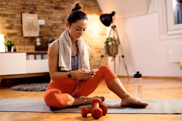 Athlète féminine utilisant un téléphone intelligent tout en se relaxant sur le sol à la maison