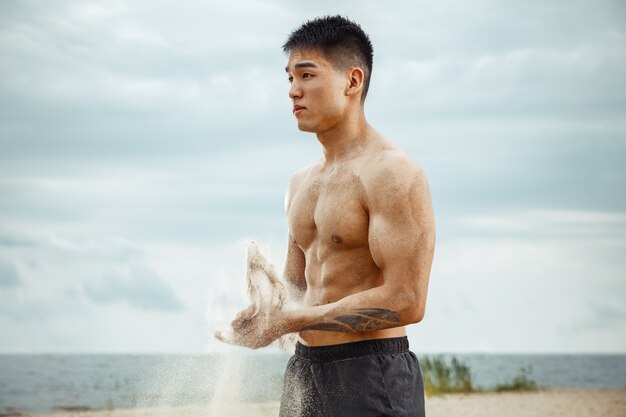 Athlète jeune homme en bonne santé, faire de l'exercice à la plage. Signle modèle masculin air d'entraînement torse nu au bord de la rivière en journée ensoleillée. Concept de mode de vie sain, sport, fitness, musculation.