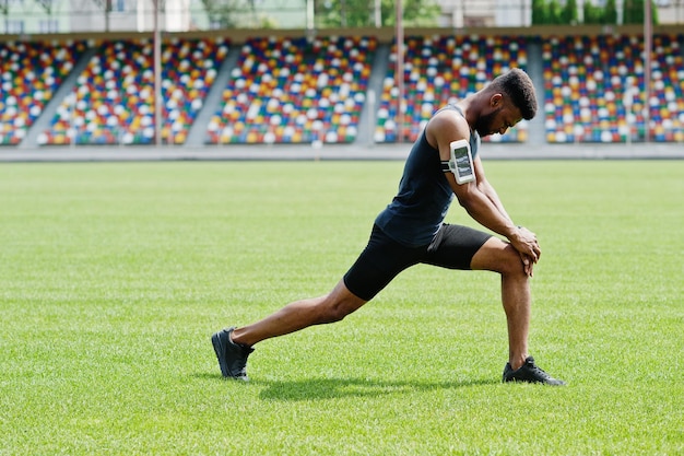 Athlète masculin afro-américain en vêtements de sport faisant des exercices d'étirement au stade