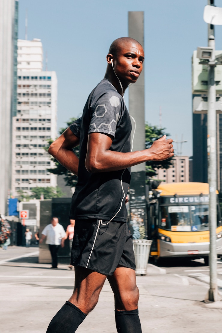 Photo gratuit un athlète masculin confiant fit jeune homme jogging sur route en écoutant de la musique sur des écouteurs