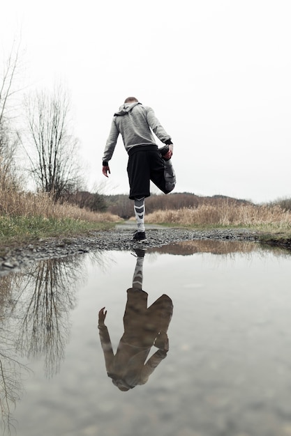 Athlète masculin étirant sa jambe près de la flaque d&#39;eau