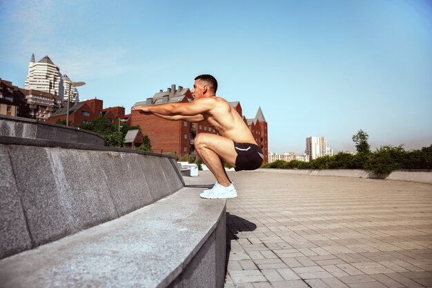 Un athlète masculin musclé faisant de l'exercice dans le parc. Gymnastique, entraînement, flexibilité des entraînements de fitness. Ville d'été en journée ensoleillée sur le terrain de fond. Mode de vie actif et sain, jeunesse, musculation.