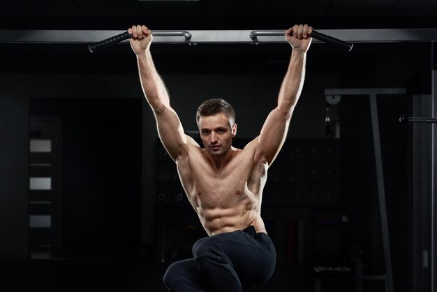 Athlète masculin musclé tirant sur la barre horizontale dans une salle de sport sombre