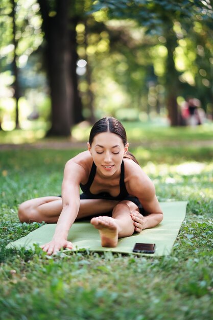 Athlétique jeune femme faisant du yoga dans le parc le matin, la formation des femmes sur un tapis de yoga