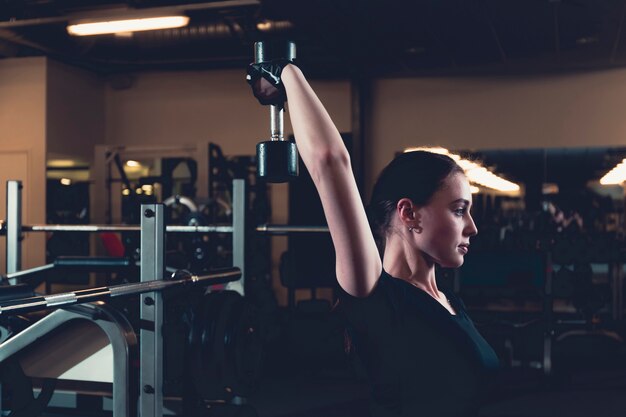 Athlétique jeune femme faisant des exercices triceps avec haltère dans un centre de fitness