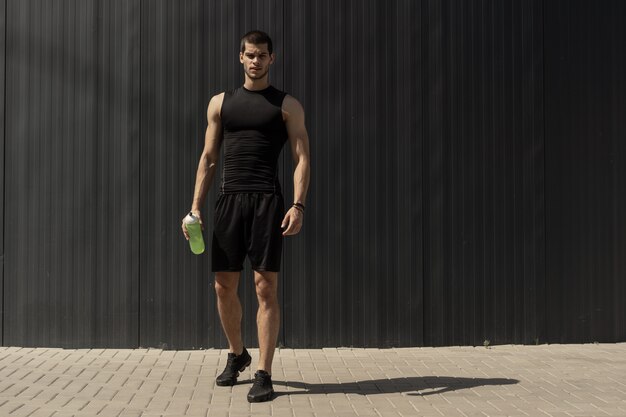 Athlétique jeune homme moderne posant sur un mur métallique gris