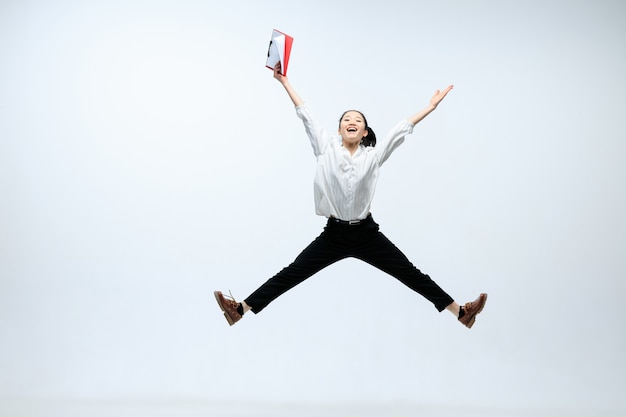 Atteignez de nouveaux sommets pour votre famille. Heureuse femme travaillant au bureau, sauter et danser dans des vêtements décontractés ou costume isolé sur fond de studio blanc. Entreprise, start-up, concept d'espace ouvert de travail.