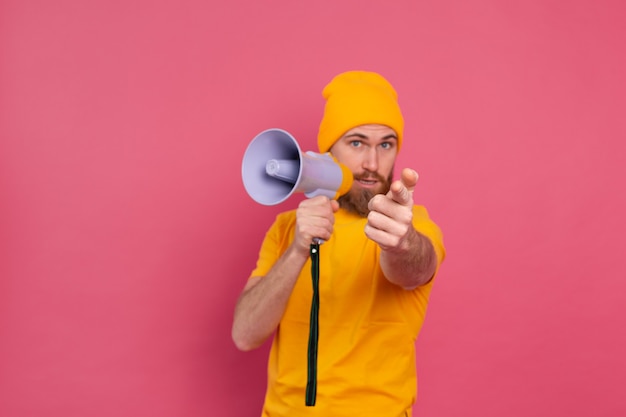 Attention! Homme européen avec mégaphone doigt pointé vers la caméra sur fond rose