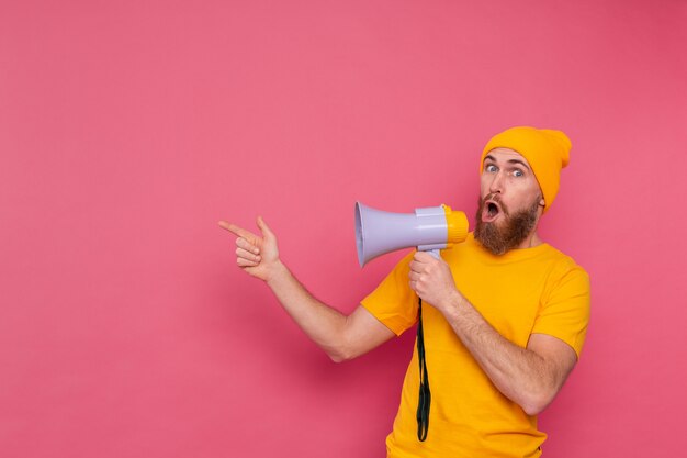 Attention! Homme européen avec mégaphone doigt pointé vers la gauche sur fond rose