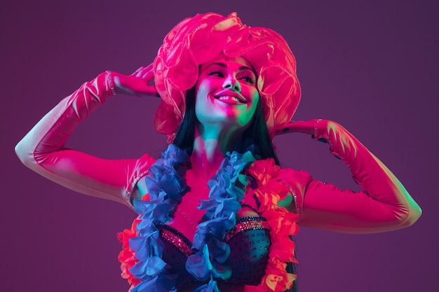 Attractif. Modèle brune hawaïenne sur mur violet en néon. Belles femmes en vêtements traditionnels souriant, dansant et s'amusant. Vacances lumineuses, couleurs de célébration, festival.