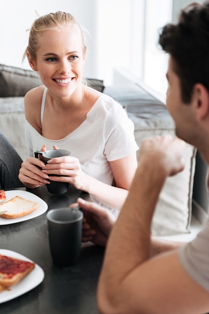 Attractive cheerful lady regardant son homme pendant qu'ils prennent le petit déjeuner