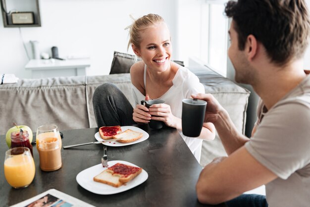 Attractive cheerful lady regardant son homme pendant qu'ils prennent le petit déjeuner