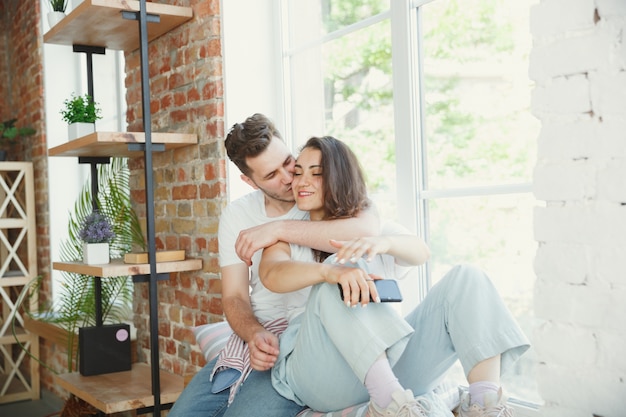 Attrapons ce moment. Jeune couple a déménagé dans une nouvelle maison ou un nouvel appartement. Ayez l'air heureux et confiant. Famille, déménagement, relations, premier concept de maison. Assis près de la fenêtre, étreignant et faisant un selfie.