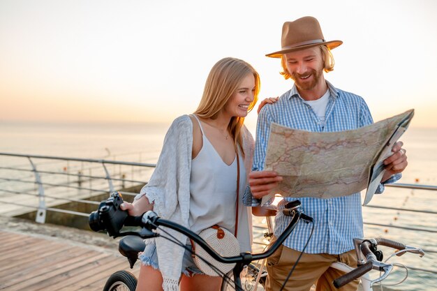 Attrayant couple heureux d'amis voyageant en été sur des vélos, homme et femme aux cheveux blonds mode style hipster boho s'amusant ensemble